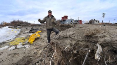一名暴风雨保护工人站在阿拉斯加纳帕基亚克的Yupik Eskimo村庄的岸上，在那里永久性冰冻的融化导致侵蚀和洪水。当地领导人正在考虑搬迁村庄。