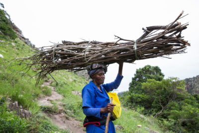 Alice Mbuthuma，他的女儿无海是采矿项目的领先对手，在穿过连接池塘的行人桥与爱德华港交叉后，携带木柴。